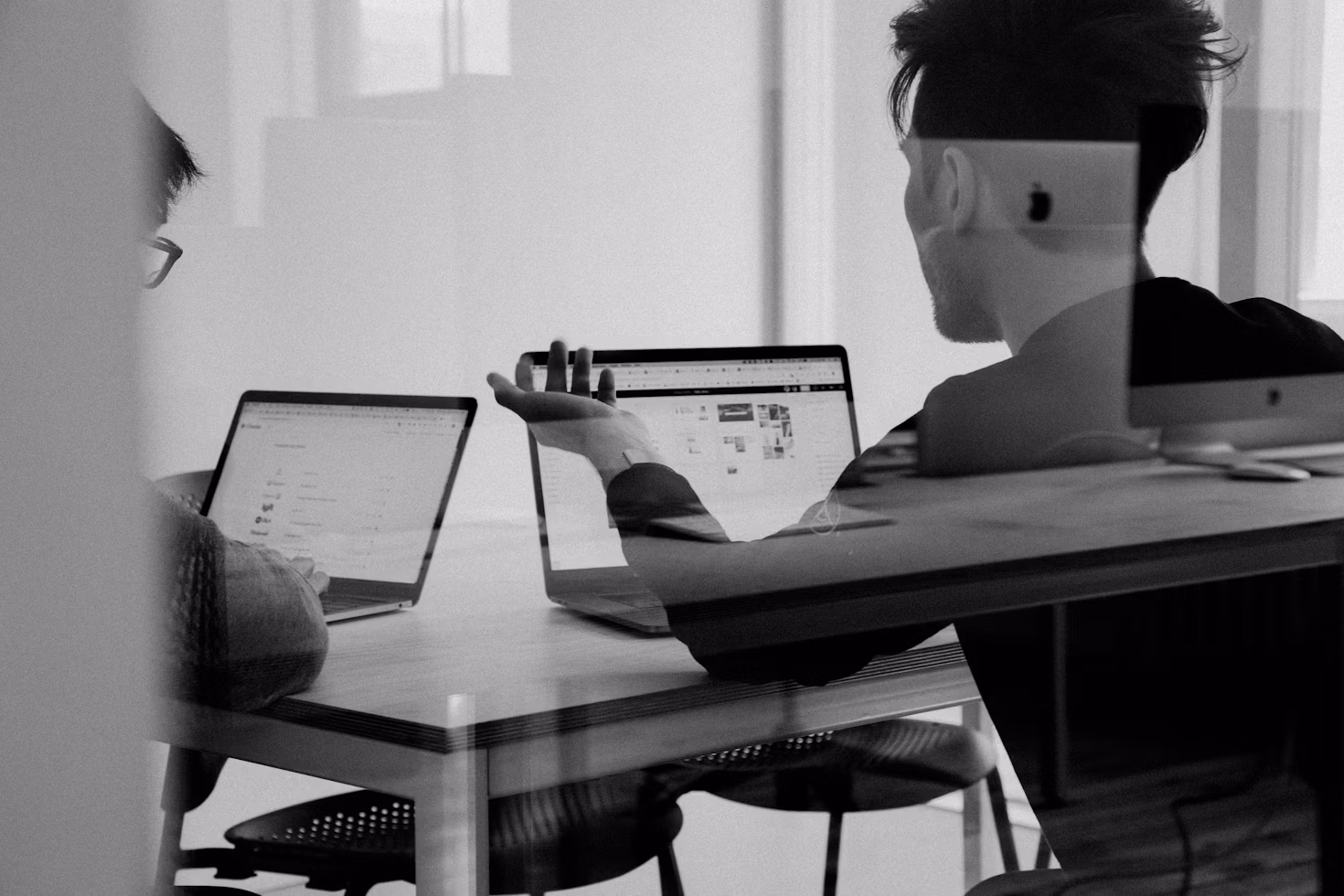 Two creative professionals collaborating in a modern office, discussing website layouts and digital design projects while reviewing work on laptops during a planning session.