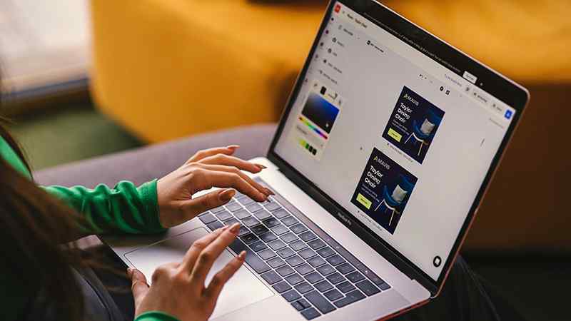 Close-up of hands typing on a MacBook laptop displaying a graphic design interface with color picker and marketing template previews, set in a casual indoor environment