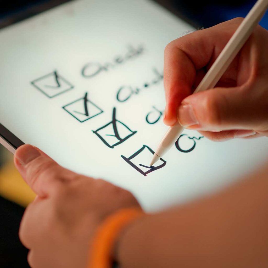 Hand marking completed items on a rebranding checklist using a stylus on a tablet, representing the step-by-step rebranding process