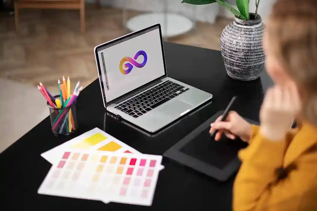 aBrand designer at work on a laptop logo design, reviewing color swatches and using a graphics tablet — creative branding and identity process