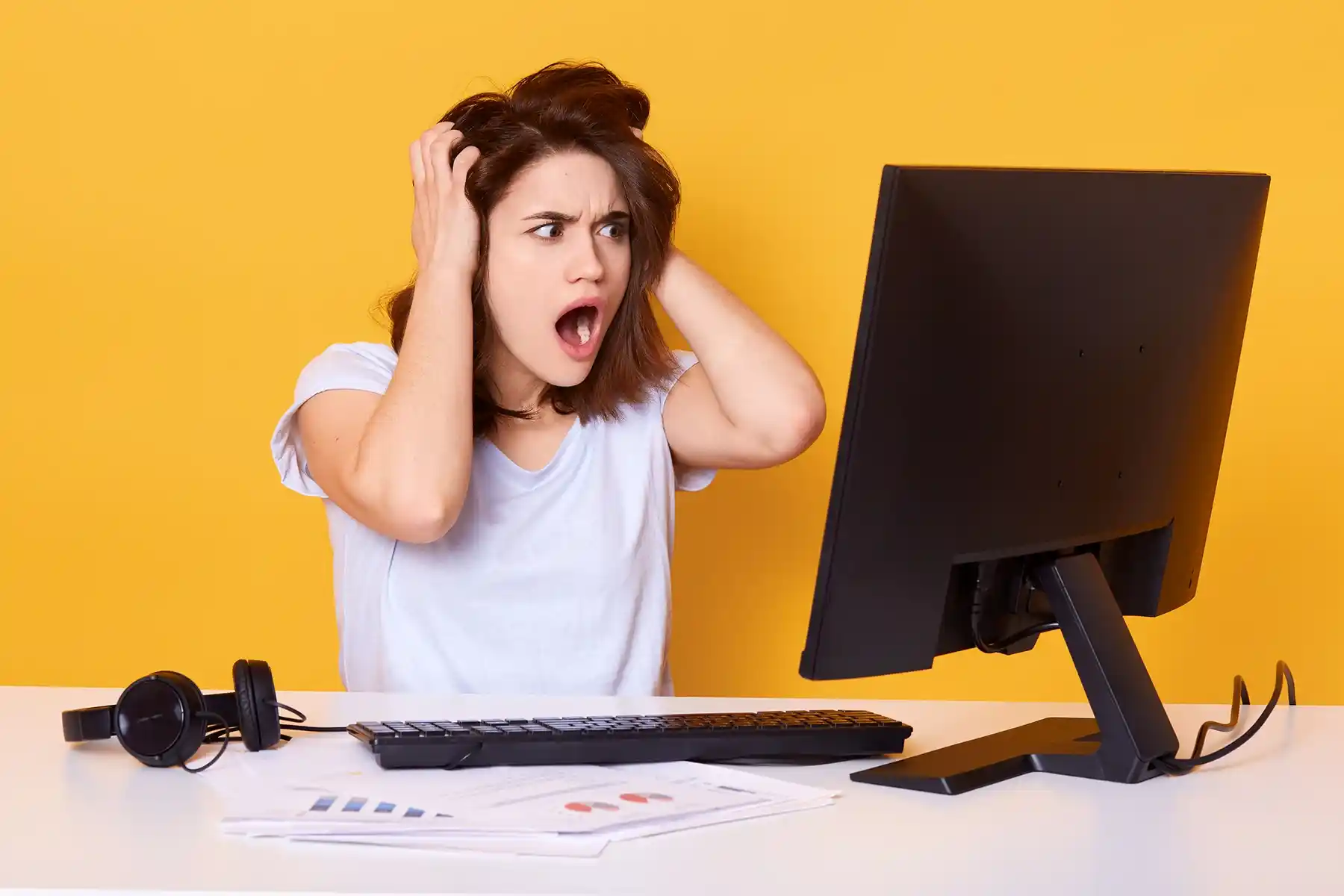 Overloaded in-house designer reacting to growing backlog, missed deadlines, and work piling up — the bottleneck that drives businesses to seek outsourced graphic design support